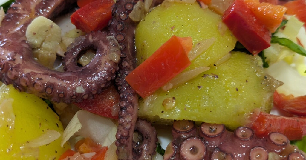 A plate of octopus, with potatoes, onions, kale and red pepper.