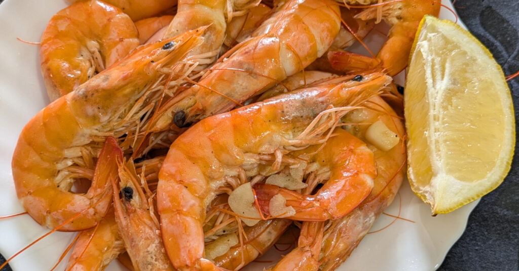 A plate of garlic prawns, served with a lemon wedge.
