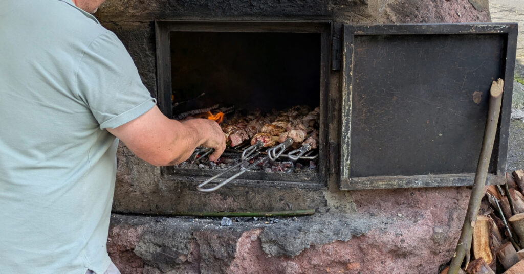A man cooks giant espetadas (meat skewers) over a charcoal fire.